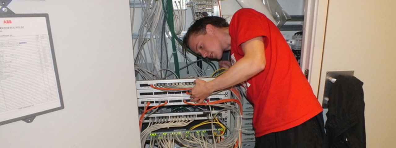 Bilete viser ein gut i raud skjorte som jobbar med ein elektrisk installasjon,