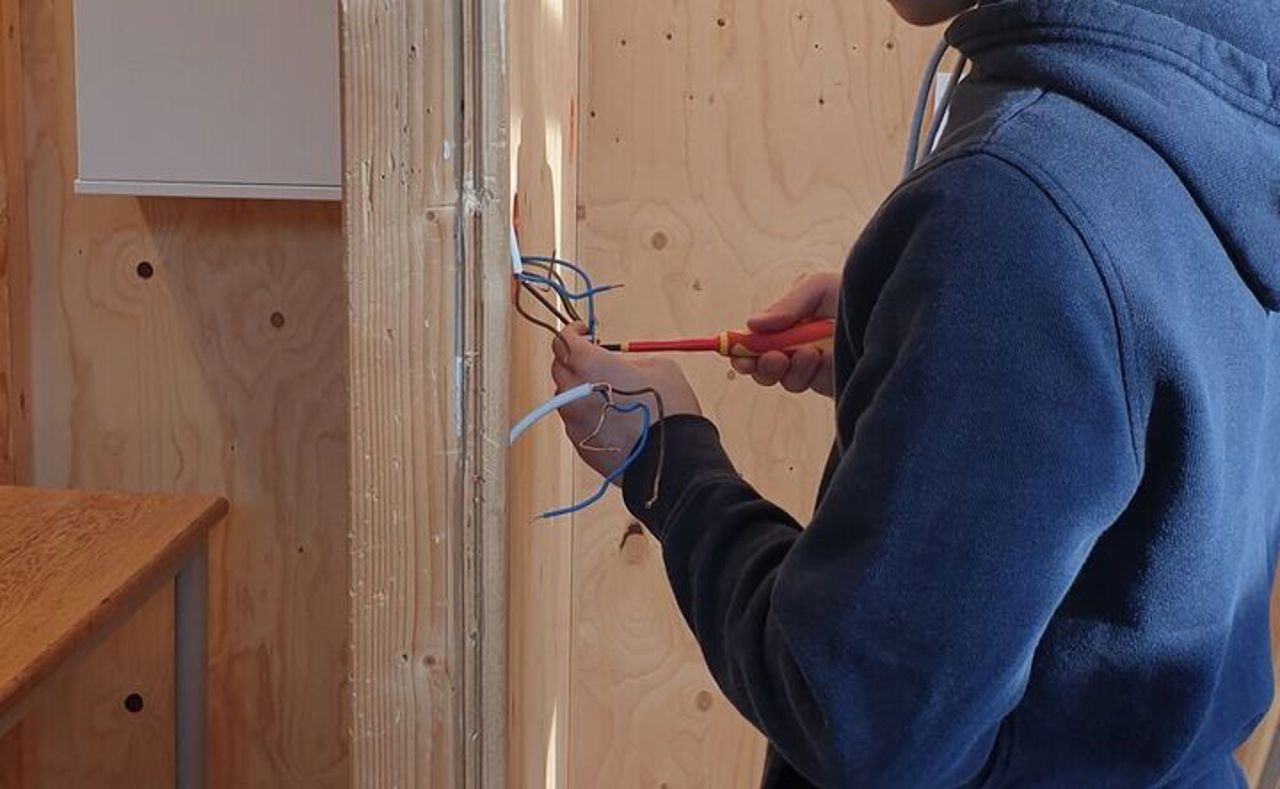 Bilete viser ein person i blå jakke som monterer ein lysbrytar på ein vegg.